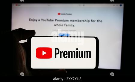 Person, die ein Mobiltelefon mit dem Logo des Video-Streaming-Abonnementdienstes YouTube Premium vor der Unternehmenswebseite hält. Schwerpunkt auf dem Display des Telefons. Stockfoto