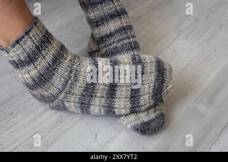 Herrenbeine in gestrickten gestreiften Socken. Stricksocken aus Wolle an überkreuzten Beinen. Warme Herbstkleidung. Gestreiftes Häkelmuster für Socken. Handgemachte Mode. Stockfoto