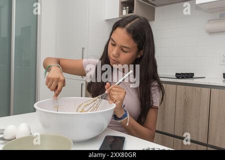 Ein junges Mädchen, das in der Küche sitzt und Zutaten mischt. Stockfoto