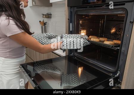 Eine junge Frau, die zu Hause rohe Kekse auf den Ofen legt. Stockfoto