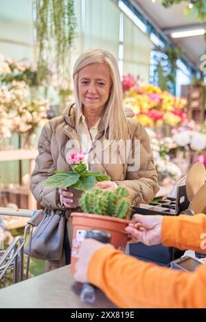 Frau mittleren Alters in einem Blumenladen, die für Pflanzen bezahlt Stockfoto