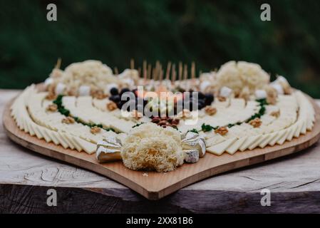 Herzförmiges Holzbrett mit verschiedenen Käsesorten und Beilagen Stockfoto