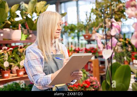 Eine Frau mittleren Alters, die in einem Kinderzimmer arbeitet, Inventar in einem Notizbuch aufnimmt. Frau mittleren Alters, die in einem Blumenladen arbeitet. Stockfoto