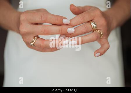 Frau in modernem weißem Kleid. Konzentriere dich auf ihre Hände mit goldenen Ringen Stockfoto