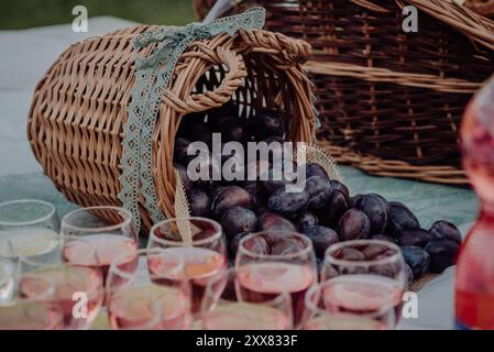 Korb gefüllt mit frischen Pflaumen neben Gläsern mit Fruchtgetränken. Stockfoto