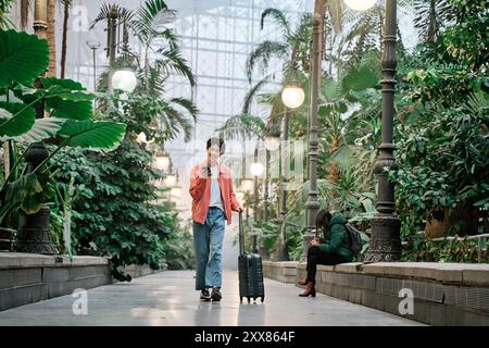 Junger asiatischer Mann, der mit einer Reisetasche auf sein Smartphone schaut Stockfoto