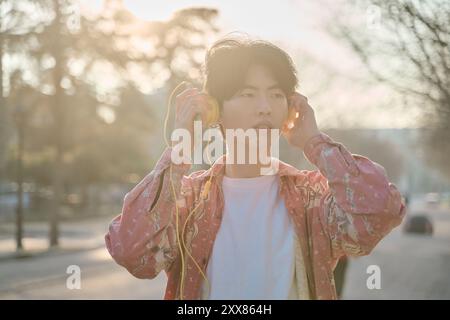 Fröhlicher, glücklicher junger asiatischer Mann, 20 Jahre alt, trägt Hemd, hört Musik in den Kopfhörern Stockfoto