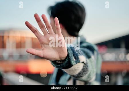 Junger asiatischer Mann, der sein Gesicht mit einem Stoppschild bedeckt. Junge Berühmtheit, die sein Gesicht mit der Handfläche bedeckt und wegblickt, um Paparazzi zu vermeiden. Stockfoto