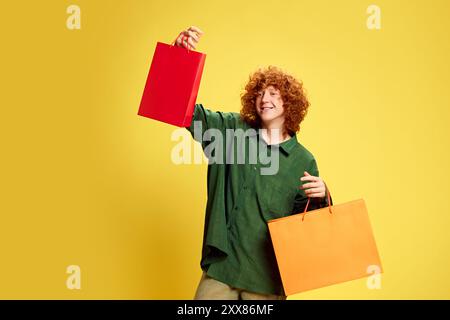 Glücklicher, stilvoller junger Mann, der eine bunte Tasche mit Kopierraum hält, um Ihren Text vor gelbem Hintergrund einzufügen. Konzept des Black Friday Stockfoto