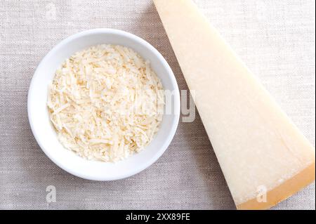 Geriebener Parmesankäse, Parmigiano Reggiano in einer Holzschale auf Leinen, mit einem ganzen Stück Käse auf der rechten Seite. Italienischer Hartkäse mit Granulat. Stockfoto