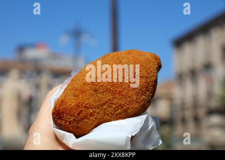 Arancini frittierte Reiskugel, typische lokale Küche in Sizilien, Italien. Catania Stadt im Hintergrund. Stockfoto