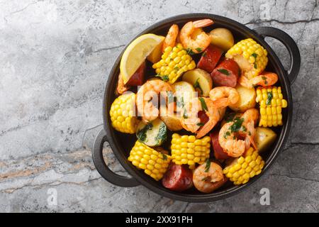 Hausgemachte Cajun Meeresfrüchte kochen mit Garnelen, Mais, Babykartoffeln, Wurst und Zitronen aus der Nähe auf dem Tisch. Horizontale Draufsicht von oben Stockfoto