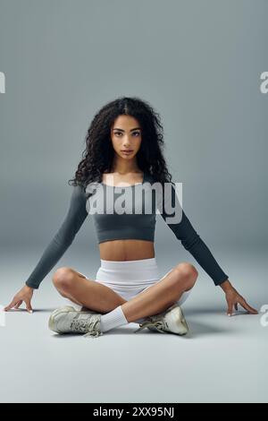 Eine junge Frau mit lockigen Haaren sitzt in entspannter Yoga-Pose und zeigt Kraft und Konzentration. Stockfoto