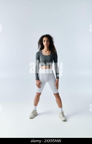 Eine junge Frau in Sportkleidung steht mit auseinander stehenden Füßen in einer Fitnessposition. Stockfoto