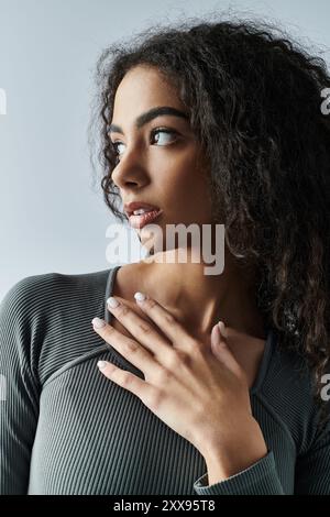 Eine junge Frau mit lockigem Haar und entschlossenem Blick steht in einem Studio, ihre Hand liegt auf der Brust. Stockfoto