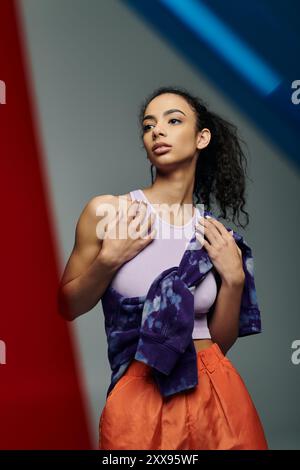 Eine junge, schöne schwarze Frau in sportlicher Kleidung steht in einem Studio mit farbenfroher Beleuchtung, die Selbstvertrauen und Energie ausstrahlt. Stockfoto