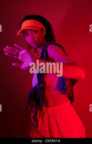 Eine junge Frau mit dunklen lockigen Haaren und einem hellorangefarbenen Visier posiert in einem neonhellen Studio. Stockfoto