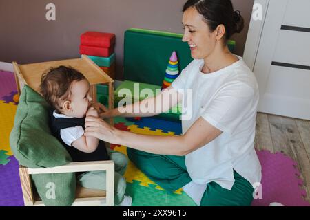 Physiotherapeut hilft einem Jungen mit ZNS-Schäden, die Mobilität und Koordination in einer lustigen Reha-Sitzung zu verbessern Stockfoto