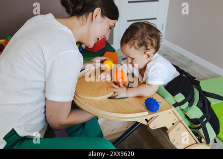 Der kleine Junge verbringt nützliche Zeit im Vertikalisierer während der Physiotherapie mit einem Physiotherapeuten. Vertikalizer für Kinder Stockfoto