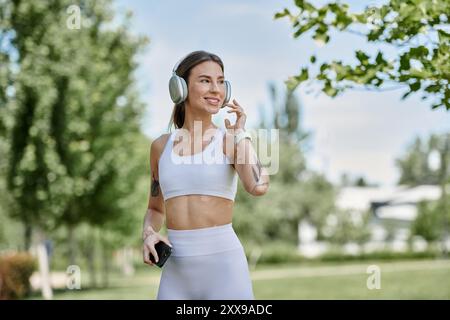 Eine junge Frau mit Vitiligo, die aktive Kleidung und Kopfhörer trägt, spaziert durch einen sonnigen Park und genießt ihr Training. Stockfoto