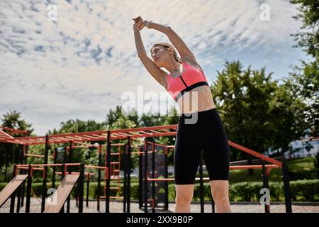 Eine junge Frau mit Vitiligo streckt ihre Arme über dem Kopf, während sie ein pinkfarbenes Crop-Top und schwarze Shorts in einem Outdoor-Park trägt. Stockfoto