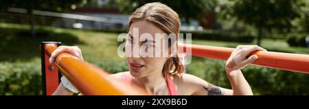 Eine junge Frau mit Vitiligo, die ein pinkfarbenes Crop Top und Aktivkleidung trägt, führt im Park eine Pull-up-Übung durch. Stockfoto