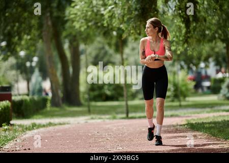 Eine junge Frau mit Vitiligo schaut auf ihrer Uhr, während sie auf einem Parkweg läuft, in einem pinken Crop Top und schwarzen Shorts. Stockfoto