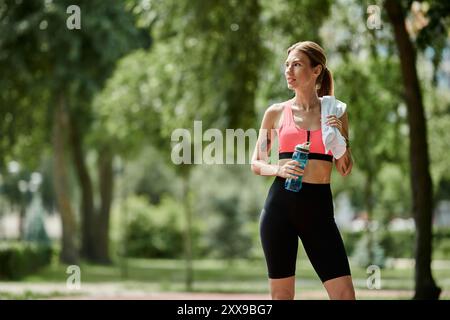 Eine junge Frau mit Vitiligo, die rosa Aktivkleidung trägt, hält nach dem Training im Park eine Wasserflasche und ein Handtuch in der Hand. Stockfoto
