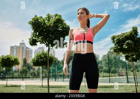 Eine junge Frau mit Vitiligo, trägt ein pinkfarbenes Crop Top und schwarze Shorts, streckt ihren Arm in einem Park. Stockfoto