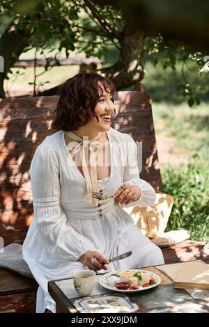 Eine junge Frau in einem weißen Kleid genießt Brunch in einem Sommergarten, umgeben von Grün. Stockfoto