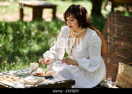 Eine junge Frau in einem weißen Kleid genießt einen gemütlichen Brunch im Freien in einem üppigen Garten. Stockfoto