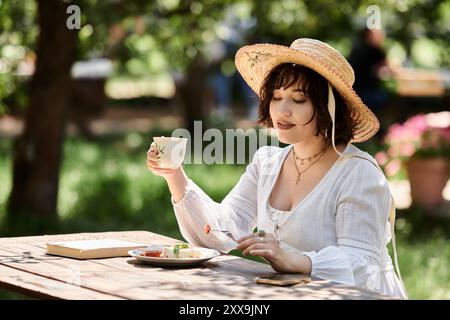 Eine Frau in einem weißen Kleid genießt einen gemütlichen Brunch in einem Sommergarten. Stockfoto