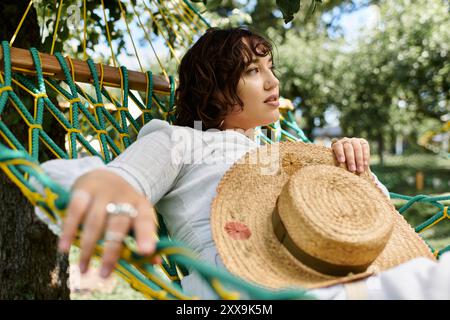 Eine junge Frau in weißem Kleid und Strohhut entspannt sich an einem sonnigen Sommertag in einer Hängematte. Stockfoto