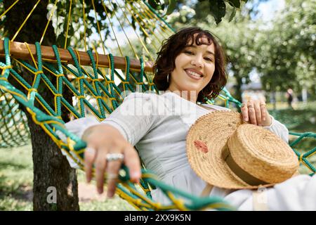 Eine junge Frau in weißem Kleid und Strohhut entspannt sich in einer Hängematte, umgeben von üppigem Grün. Stockfoto