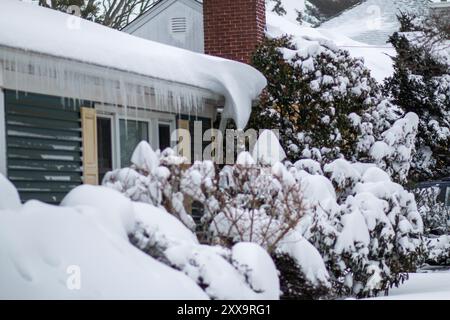 Schnee auf dem Dach eines Hauses und die Büsche im Froz mit Eiszapfen hängen vom Dach Stockfoto