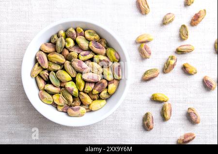 Pistazien-Kerne, geröstete und gesalzene Nüsse in einer weißen Schüssel auf Leinengewebe. Geschälte Früchte von Pistacia Vera, knusprig geröstet und gesalzen. Stockfoto