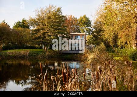 Fernsicht von der anderen Seite des Teichs auf die hintere Südhöhe des Hauses. Serenity - Scawby Brook, Scawby Brook, Großbritannien. Architec Stockfoto