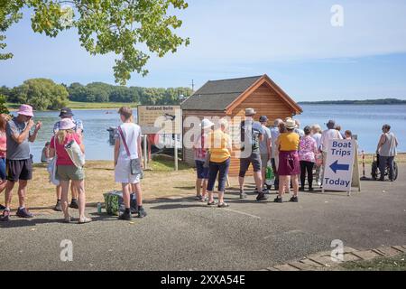 An einem Sommertag wartet eine ordentliche Warteschlange auf Sie, um an Bord des Rutland Belle-Kreuzfahrtschiffes zu einer Fahrt rund um den Rutland Wasserspeicher in England zu gehen. Stockfoto