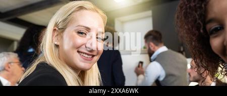 Horizontales Banner oder Kopfzeile mit junger blonder kaukasierin, die während der Arbeit mit einem multiethnischen Team im modernen Büro in die Kamera schaut - Coworking con Stockfoto