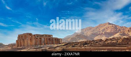 Weitwinkelblick auf das Ramesseum, den Leichentempel von Pharoah Ramesses II. Dem Großen mit der Kulisse der thebanischen Hügel an einem hellen Nachmittag mit blauem Himmel in Luxor, Ägypten Stockfoto