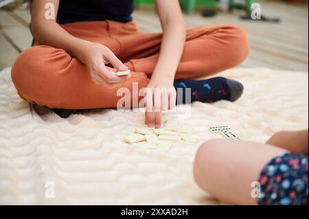 Kinderhände setzen sich mit Domino-Fliesen auf einer gemütlichen Decke auseinander und fördern spielerische Interaktion und Kreativität in einer beruhigenden Atmosphäre. Stockfoto