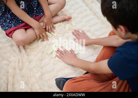 Kinder spielen mit Dominos auf einer Decke ein lustiges Spiel, fördern die Kreativität und spielen in einer warmen, komfortablen Umgebung. Stockfoto