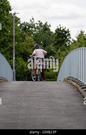 Ein Bauarbeiter mit Helm schiebt sein Fahrrad nach der Arbeit über eine Brücke Stockfoto