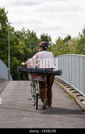 Ein Mann mit Helm schiebt sein Fahrrad mit großen Kisten, die an den Rücken geschnallt sind, auf einem Brückenweg hoch Stockfoto