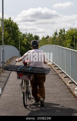 Ein Mann mit Helm schiebt sein Fahrrad mit Vogelkäfigen, die an einem sonnigen Tag nach hinten über eine Brücke geschnallt sind Stockfoto