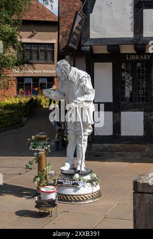 Der mit weißer Farbe bedeckte Straßenkünstler posiert auf einem Sockel und unterhält Touristen, die shakespeares Geburtsort besuchen Stockfoto