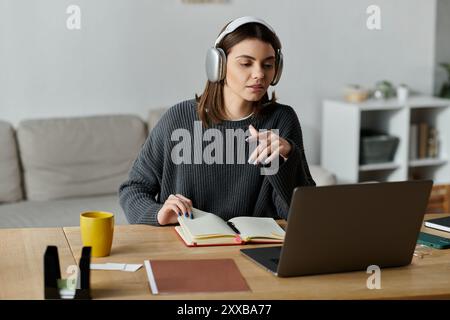 Eine junge Frau arbeitet von zu Hause aus, trägt Kopfhörer und verwendet ein Notebook, um Inhalte zu erstellen und digitale Marketingkampagnen zu verwalten. Stockfoto