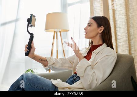 Junge Frau filmt Vlog im Wohnzimmer mit Smartphone-Stabilisator. Lässig gekleidet, engagiert sie sich mit ihrem Publikum. Stockfoto