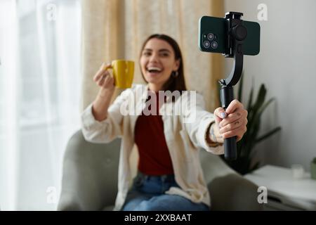 Eine junge Frau, lässig gekleidet, vloggt sich, während sie einen Smartphone-Stabilisator hält, um Videoinhalte zu erstellen. Stockfoto