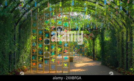 Schlendern Sie während des Sommerfestes durch den pulsierenden „Rosentunnel“, wo bunte Windspiele und verspielte Spielzeug-Windmühlen ein beruhigendes visuelles und Stockfoto